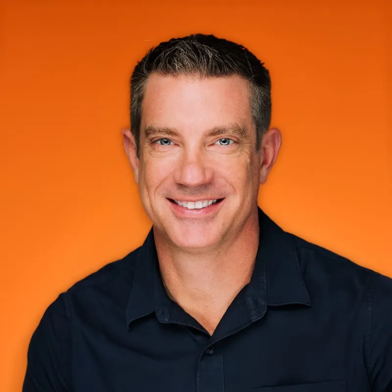 A headshot of a person wearing a black polo shirt. The person is in front of an orange background.