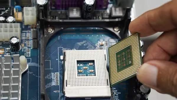 An engineer hands is shown installing a CPU processor into a socket on a computer motherboard.