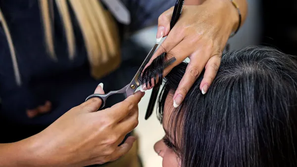 A cosmetologist works on a client's hair.