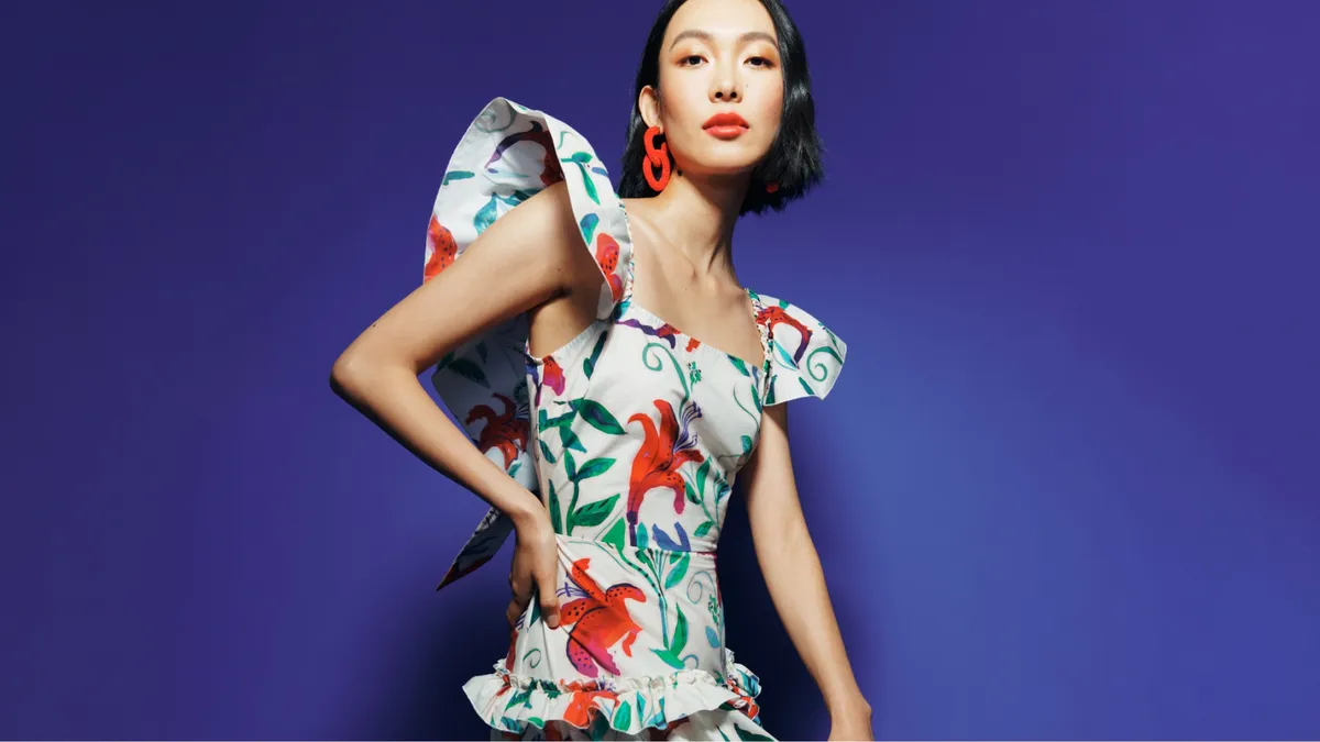 A model wears a colorful floral print frock against a bright blue background.