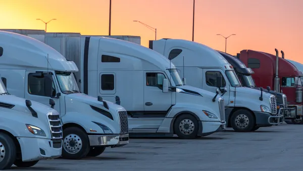 Rows of trucks parked at a rest stop against a yellow and pink sunset.