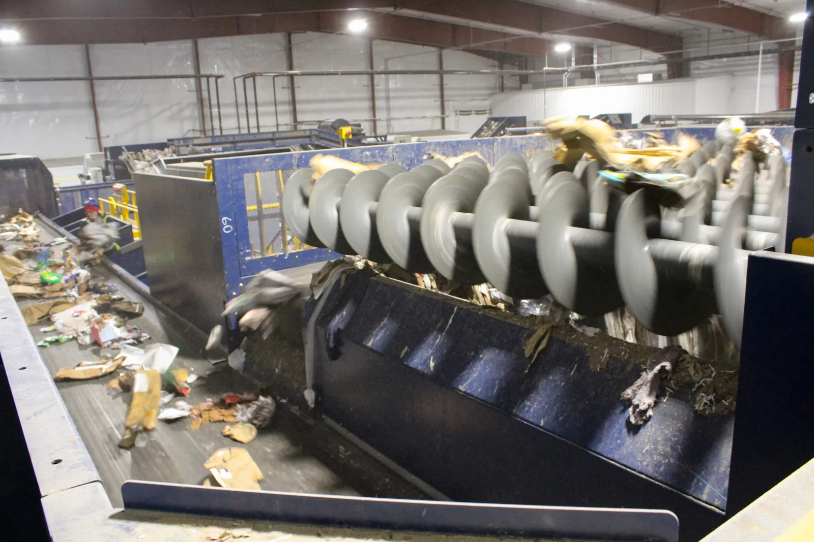 Recyclable materials moving over the top of a piece of sorting equipment and falling to a conveyor belt below.