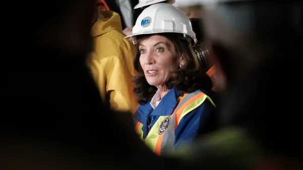 A woman wearing a white hard hat labeled "MTA" in a dark tunnel.