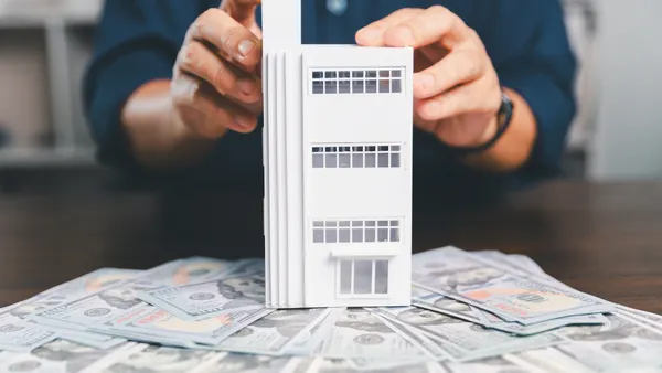 Model house, stacks of coins, calculator, financial documents on a wooden desk.