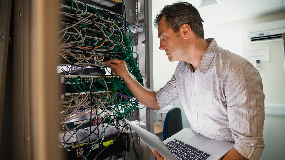 A male IT professional with a laptop in check a server stack.