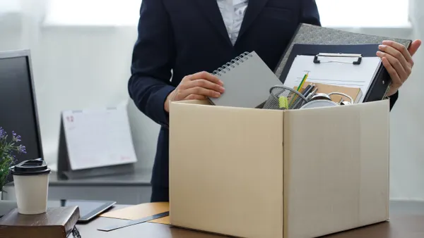 Businesswoman packs belongings into a box sitting on a desk.