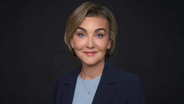 A headshot of a person in front of a blue background. The person is wearing a navy suit.