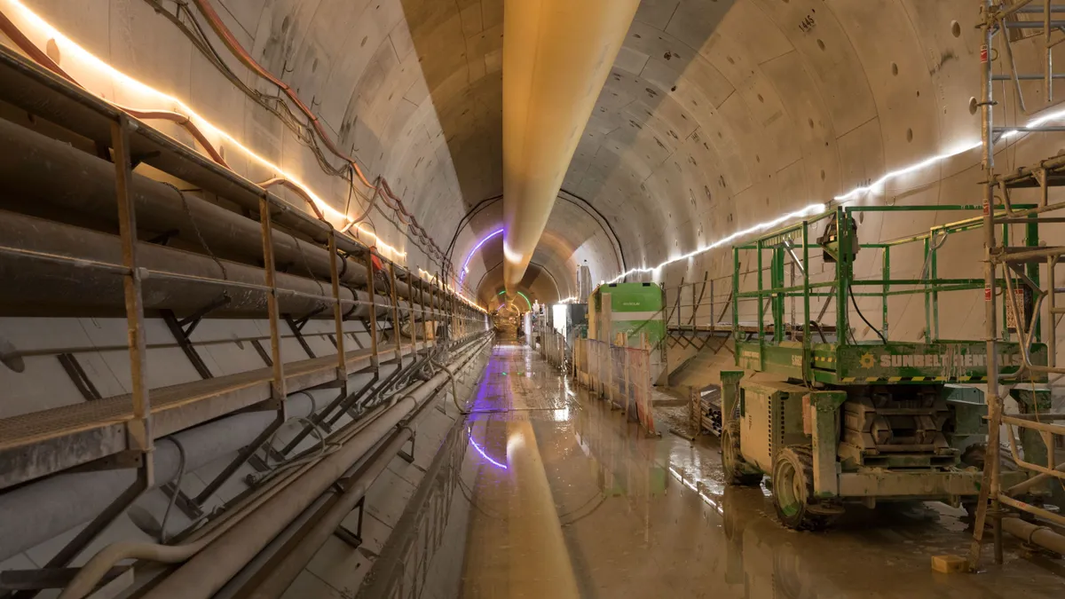 A long underground tunnel, dimly lit, is filled with all manner of construction equipment.