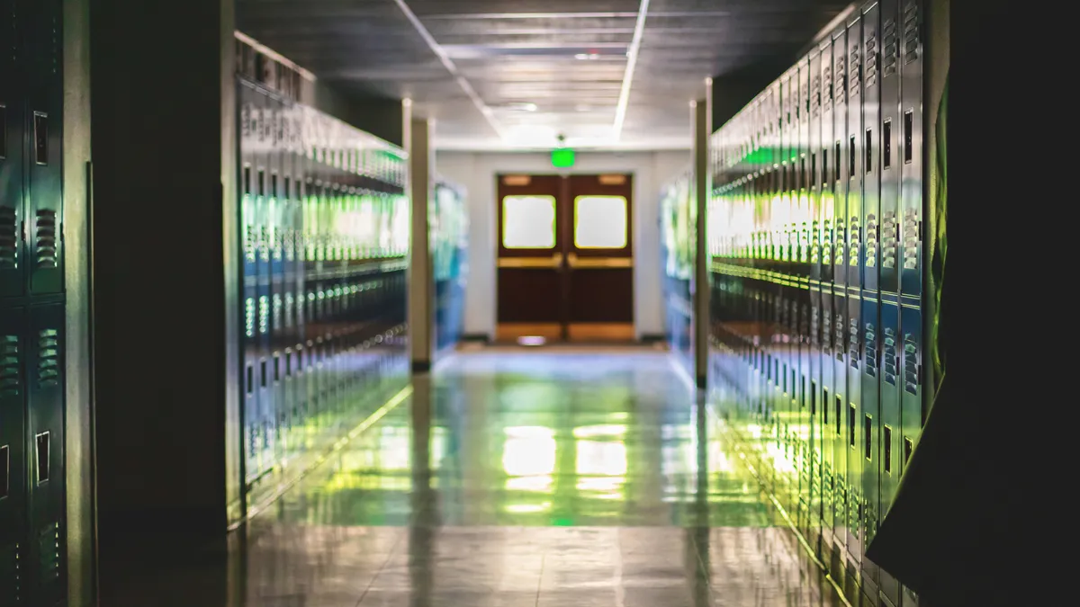 A dimly lit school hallway is empty with a row of lockers standing on each side.