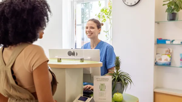 Smiling dental receptionist assisting patient at reception desk