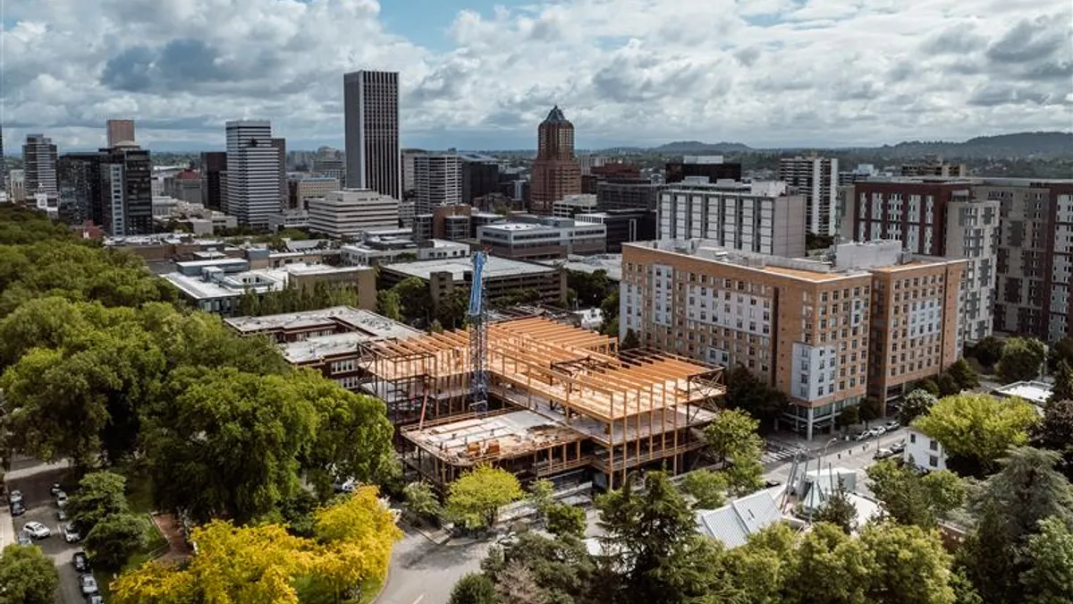 An aerial shot of an under-construction, wooden building amid a nest of other, fully constructed buildings.