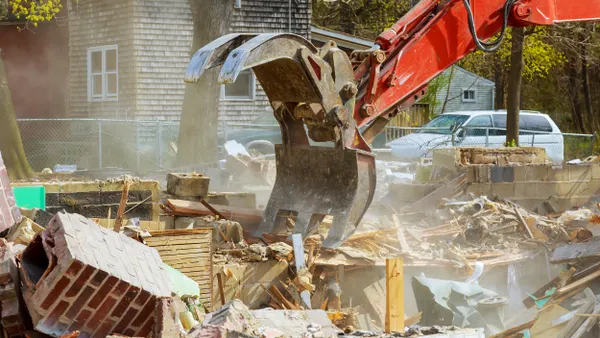 Yellow earth mover scooping up debris from demolished home.