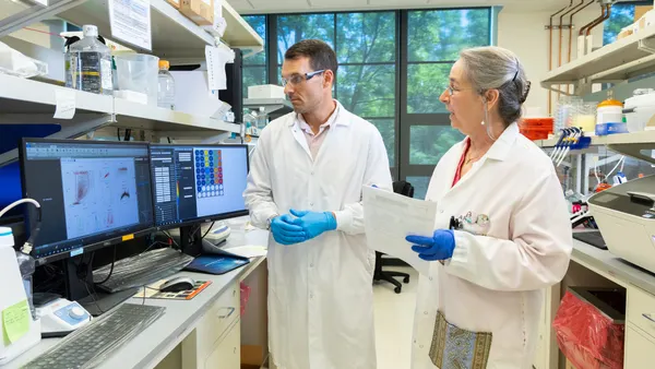 Two people in white coats stand next to a laboratory workbench