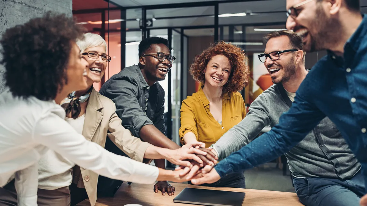 Business team members stack their hands above a table