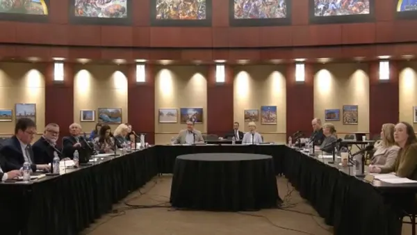 School board members sit on a U-shaped table with microphones and placards