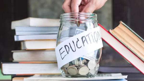 A clear glass jar sits on a pile of books. Inside the jar are bills and coins. A label on the jar says "Education"