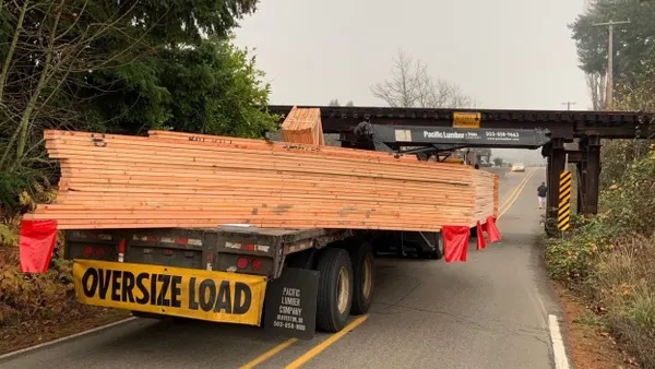 A flatbed with lumber and oversize load designation approaches a railroad crossing.