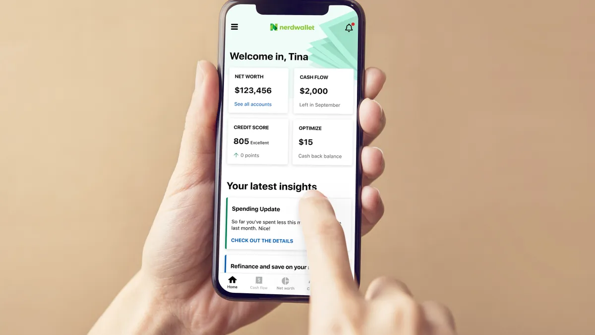 A hand holds a phone open to the Nerdwallet app tracking personal finance details