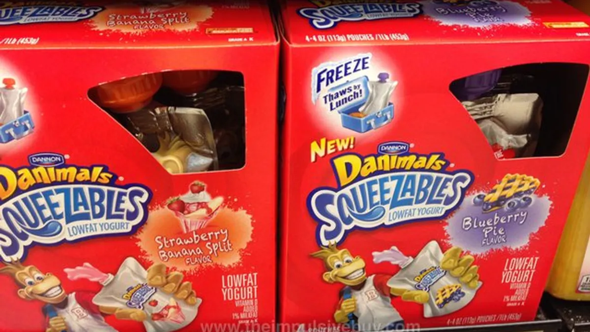 Two red boxes of squeezable Danimals yogurt in Strawberry Banana Split and Blueberry Pie flavors on a grocery store shelf.