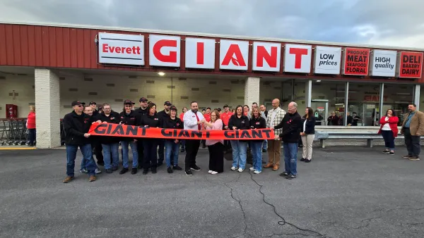 Ribbon cutting ceremony outside a grocery store with a large group of people standing behind a ribbon that says "Giant"