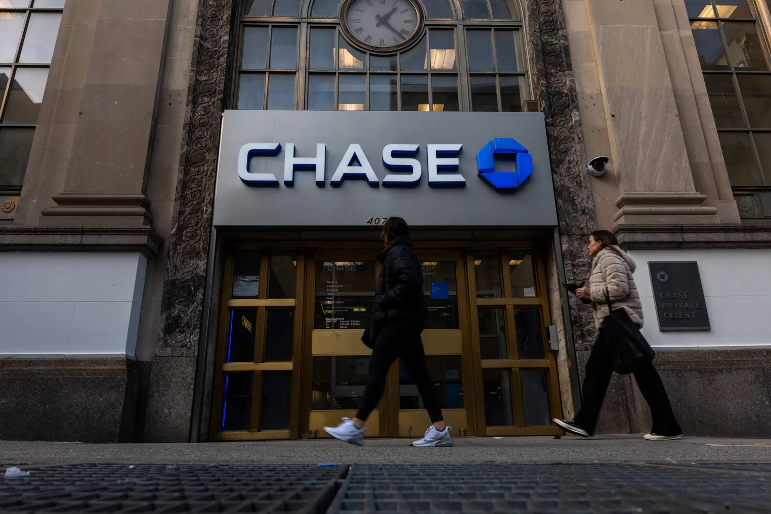 Two people walk past a Chase bank branch.