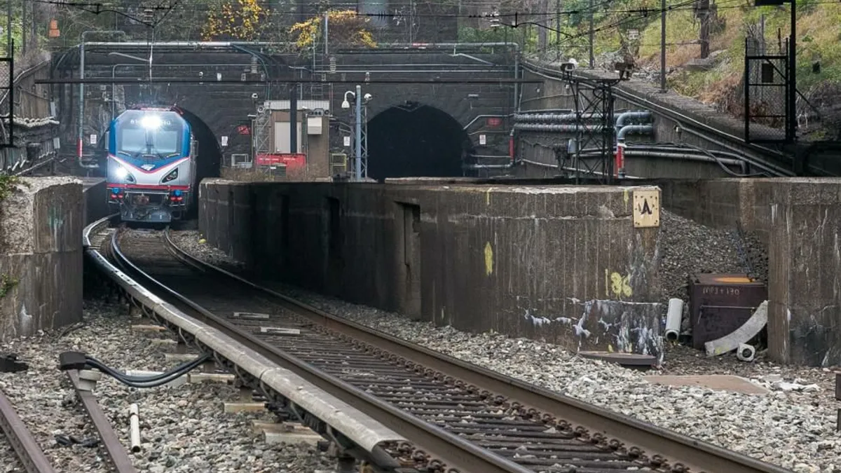 A blue and silver train emerges from a stone tunnel.