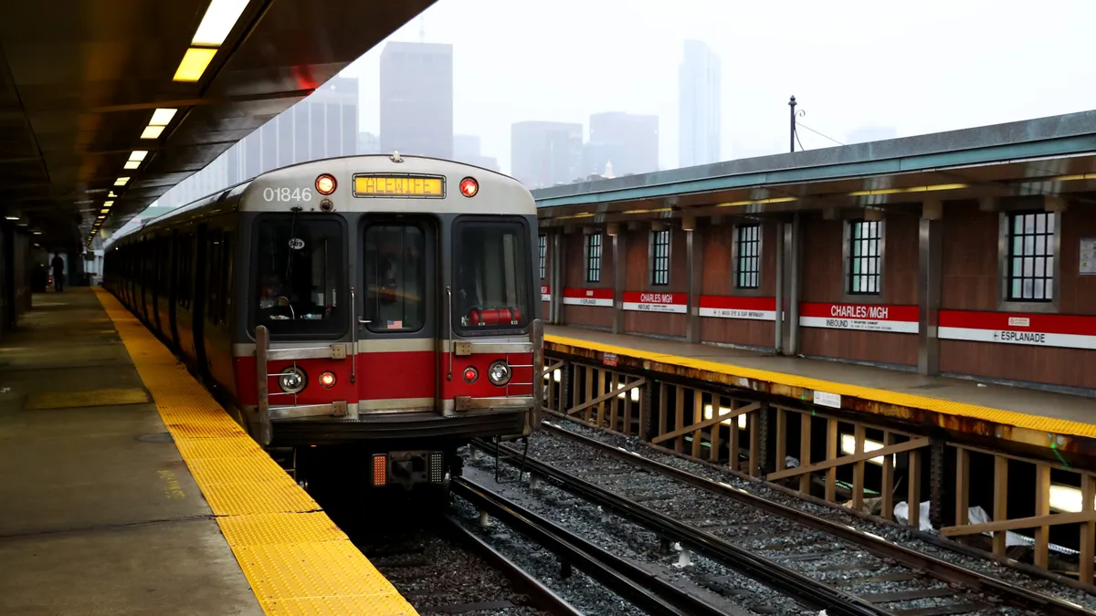 A train pulls into a elevated station in with the Boston skyline in the background.