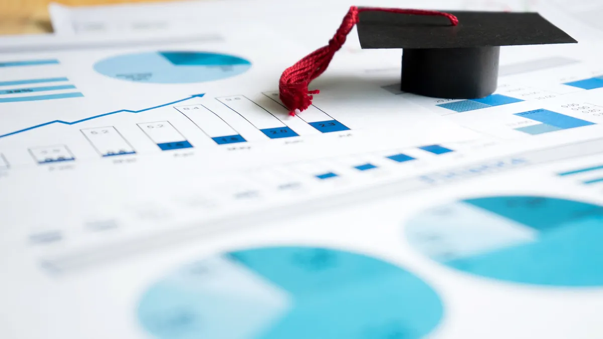 Small graduation cap on top of a piece of paper with different types of charts.