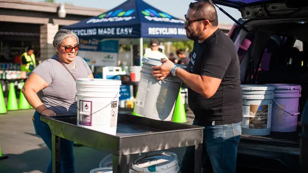 People unload paint containers from the trunk of an SUV onto a wheeled cart.
