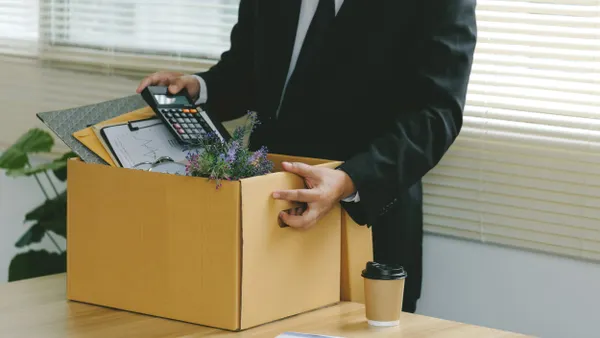 Businessman carries cardboard with office supplies.