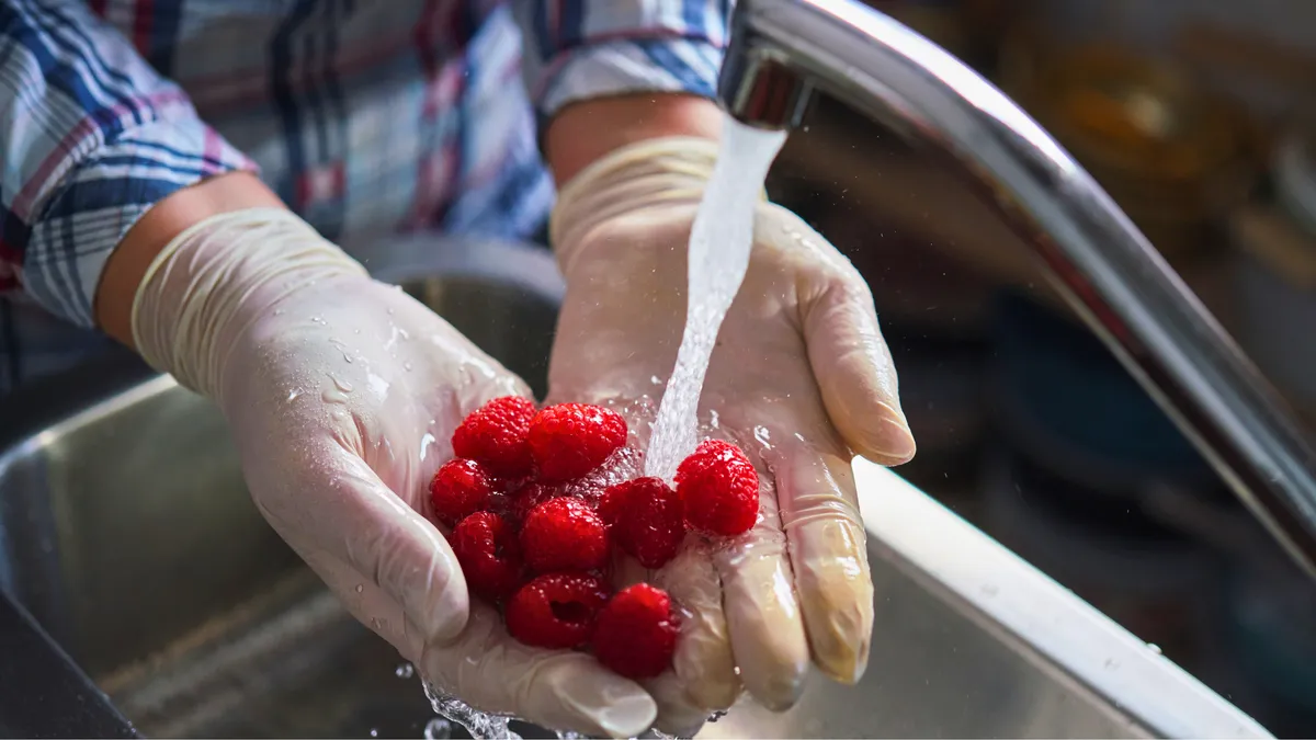 Person wearing gloves washing raspberries under running water in a sink