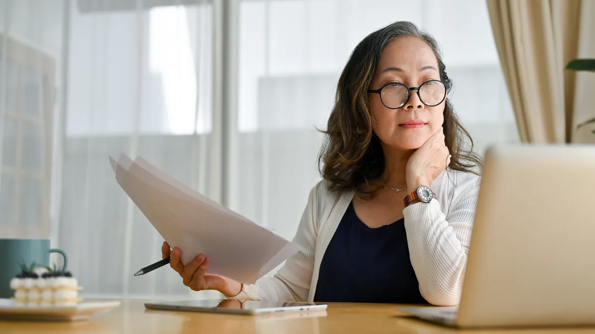 Business leader in glasses and white sweater sitting at desk using portable computer