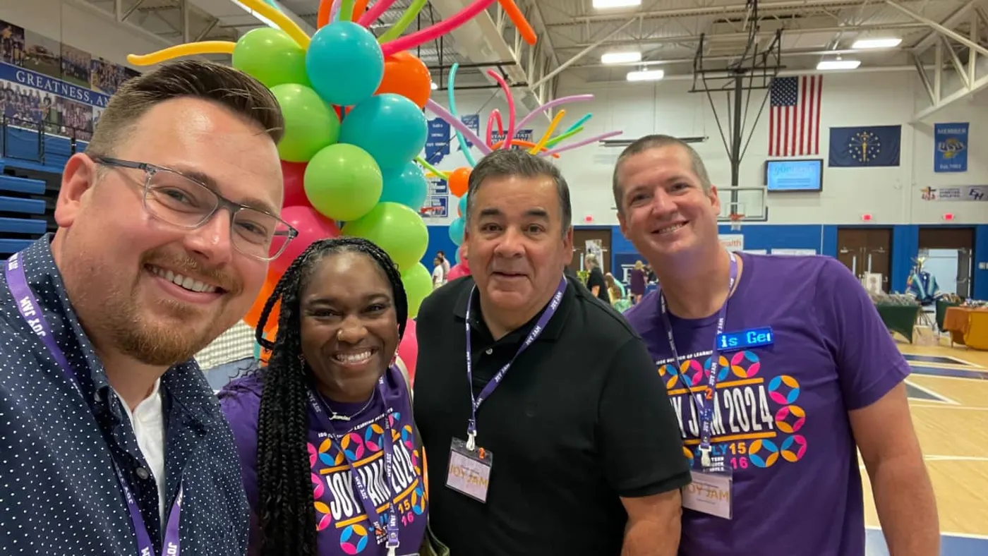 Four educators pose in a school gymnasium during a school district celebration event.