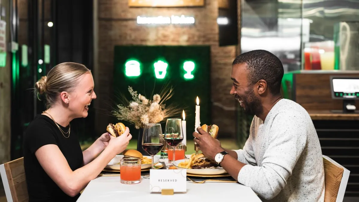 A photograph of two people at a Shake Shack eating white truffle burgers.