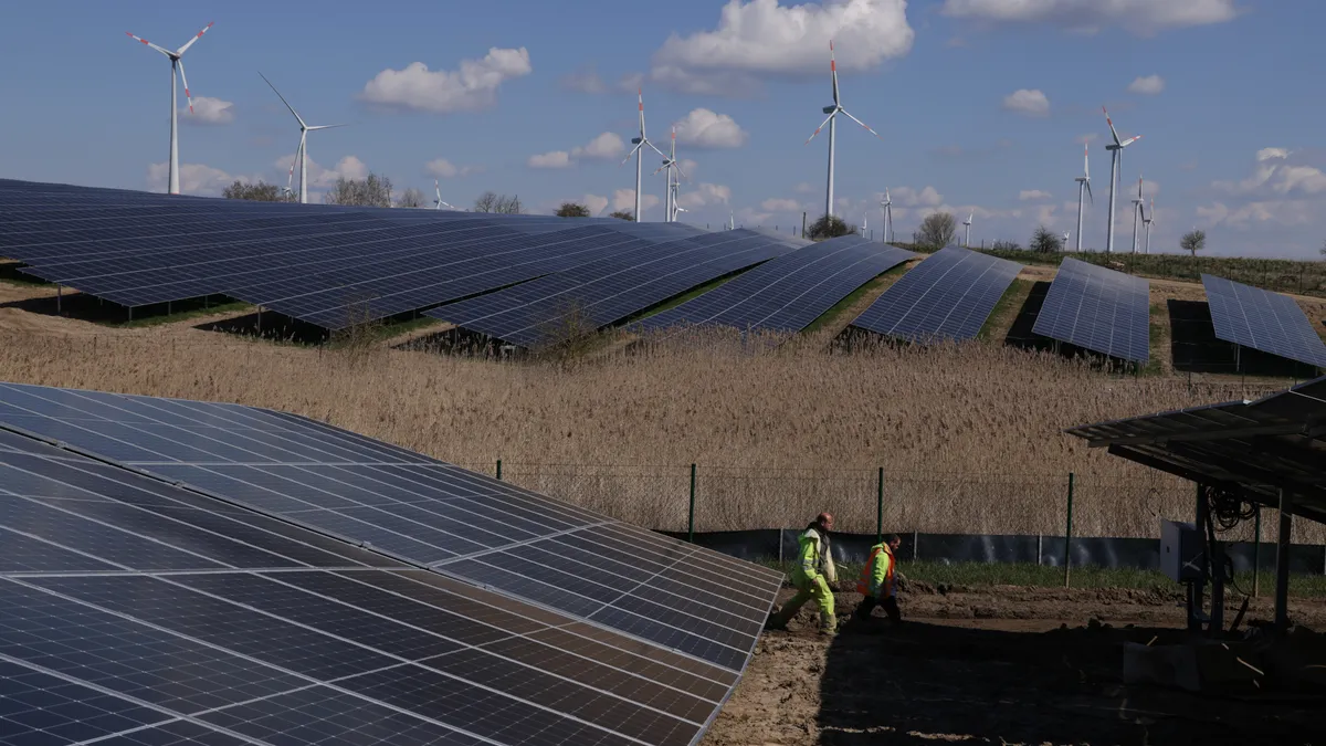 Workers walk among solar panels at the construction site of a new solar energy park as wind turbines spin behind on April 06, 2023 near Prenzlau, Germany.