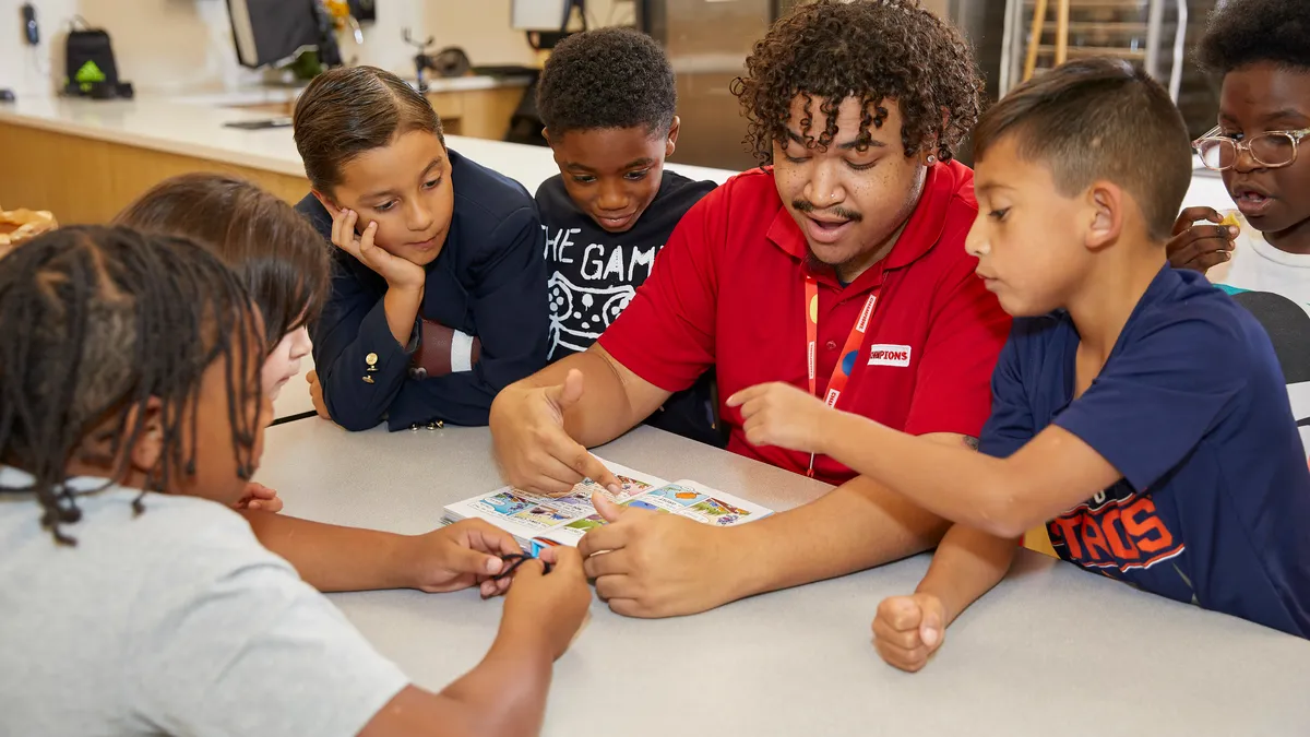 Students gathered around teacher who is reading through a book with them