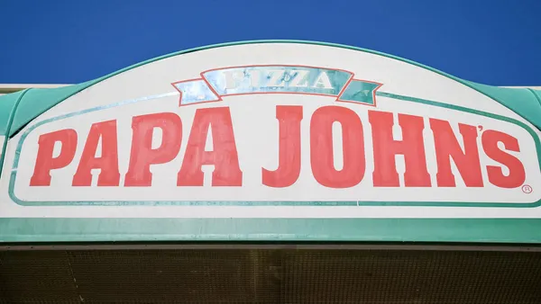 A close upimage of a Papa Johns sign with red lettering and a white background. There is green trim around the sign.