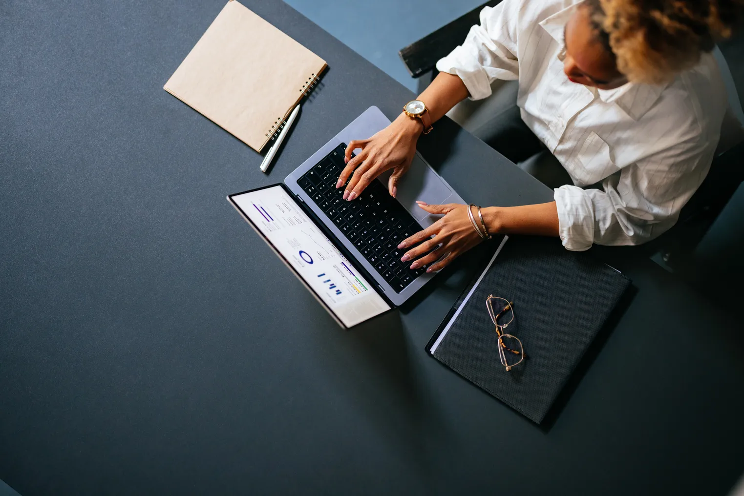 High angle view of person working on a laptop computer with notes and glasses nearby