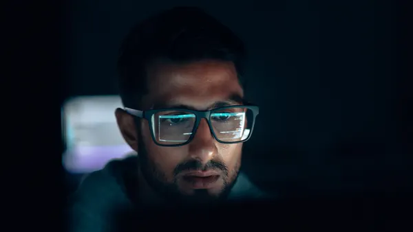a close up of a technology worker that wears glasses, looking at a monitor