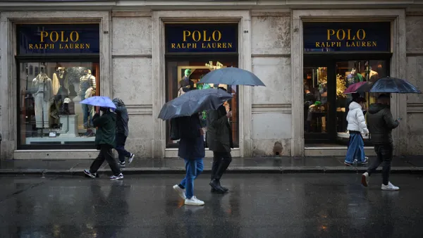 People walk in front of a Ralph Lauren storefront in the rain, carrying umbrellas.