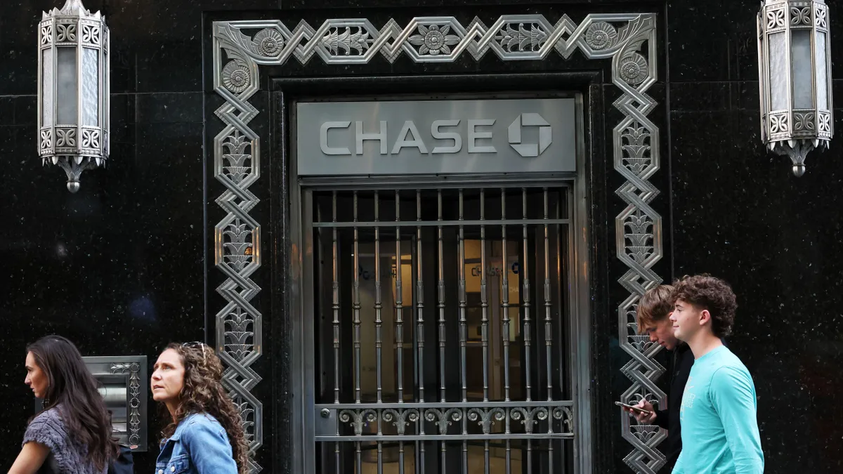 People walk on a sidewalk past an ornate door with an iron gate with the words Chase above.