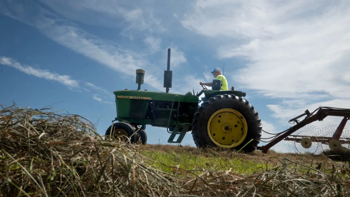 A farmer sits on a tractor with hay in the foreground