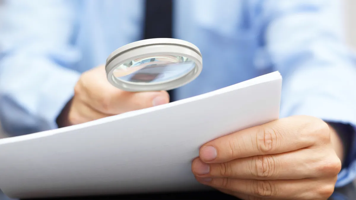 A businessperson inspects a stack of documents with a magnifying glass.