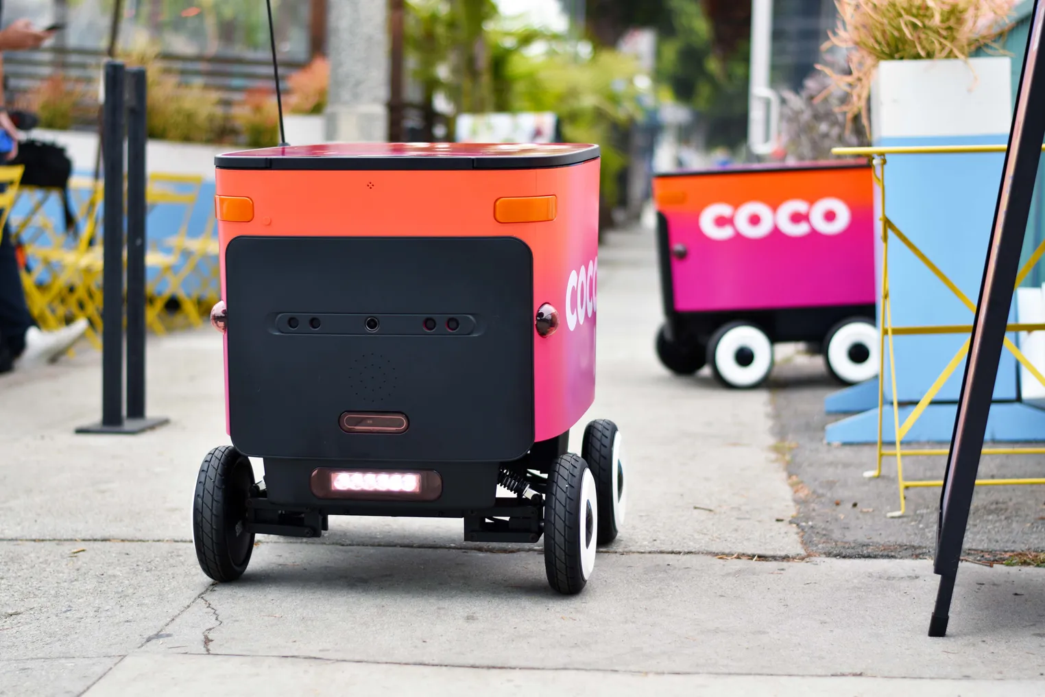 A Coco delivery robot travels along the sidewalk.