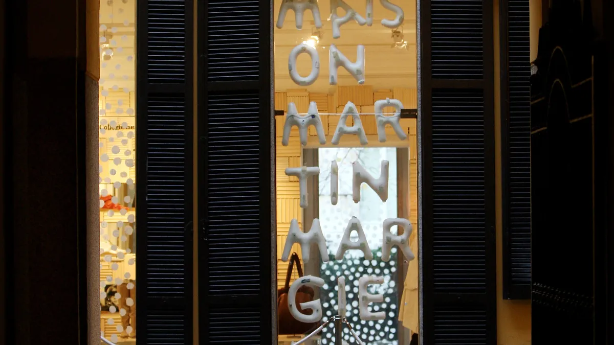 Arched doorway leading to a storefront with the words maison margiela on it. An iron chandelier hangs in the foreground.