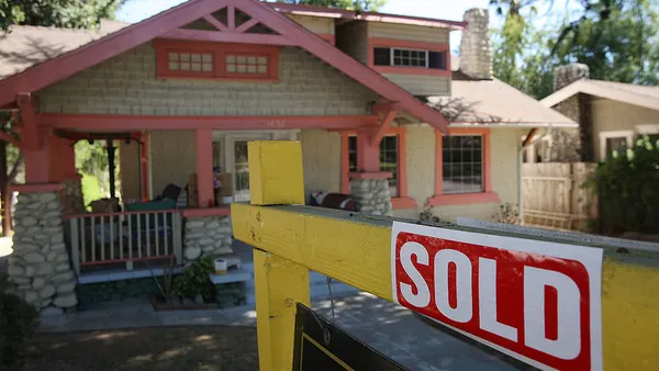 A red "sold" sign on a yellow post is in front of a small house.