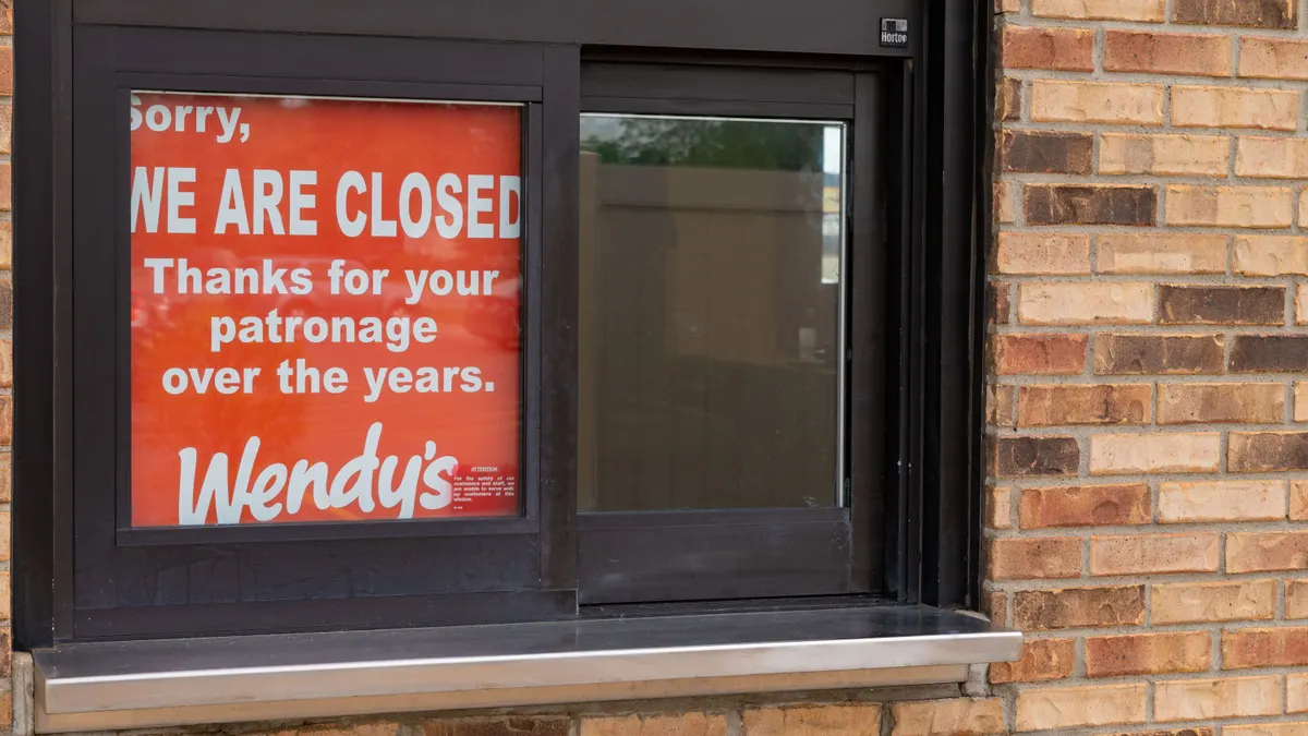 A photograph of a drive thru window with a red sign that says "Sorry, We are closed. Thanks for your patronage over the years. Wendys."