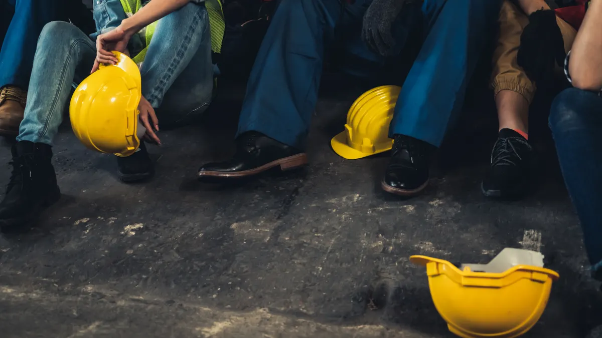 A group of people in work outfits and hard hats sit on the ground