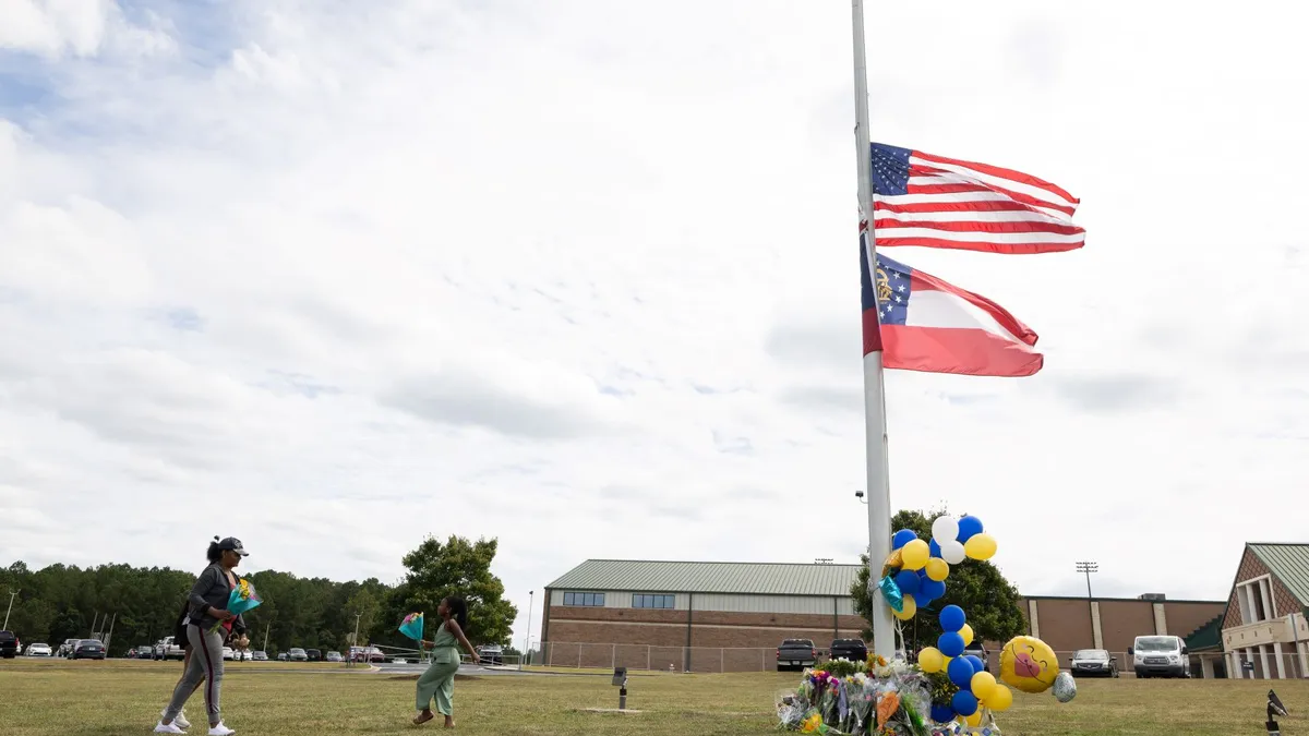 A woman approaches a flag pole with its flags half staff