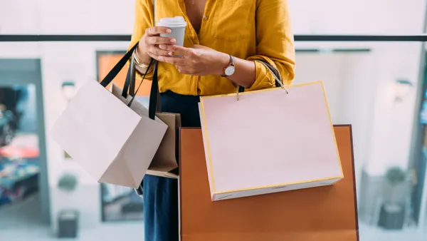 A person holds multiple shopping bags and a coffee cup.